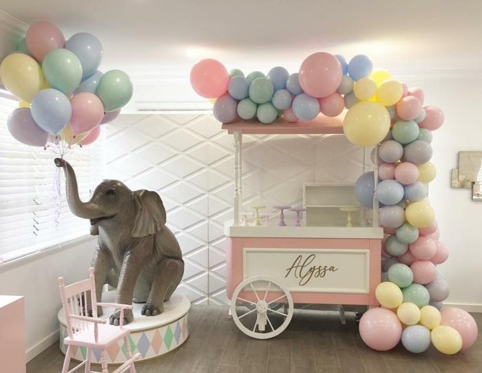 žaislas iš dramblio, nešantis galybę balionų, rožinį ir baltą vežimėlį, papuoštą arka iš įvairių dydžių ir spalvų balionų