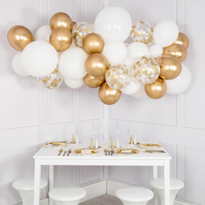 vakarėlių dekoravimo auksinių ir baltų balionų debesis, baltas stalas su baltomis ir auksinėmis plokštelėmis, blizgantys balionai