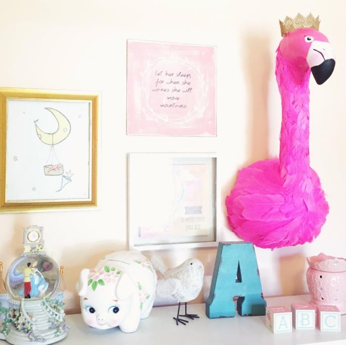 roza flamingo deco, flamingo glava v fuksijastih perjih, glava s krono v zlati barvi, stena v pastelno rumeni barvi, tri slike, ena z zlatim okvirjem, druga v belem okvirju, tretja v roza barvi