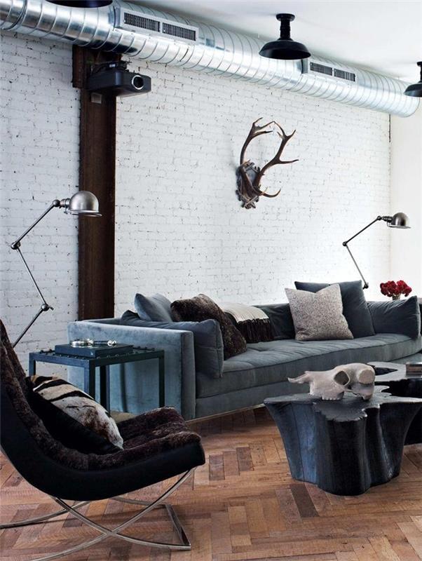 pramoniniai baldai, tamsiai mėlyna sofa, atviri vamzdžiai, dekoratyvinės pagalvėlės, metalinės lempos, baltos sienos