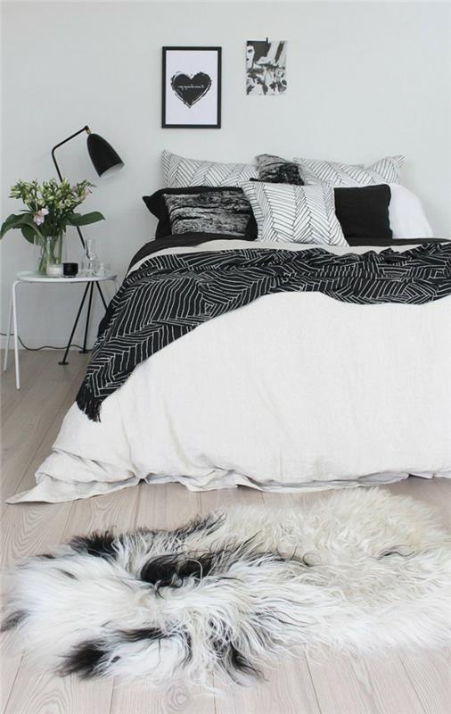 balta ir pilka lova, baltas naktinis stalas, kailinis kilimas, dažytas rėmas, medinės lentos, šviesios spalvos sienų dažai