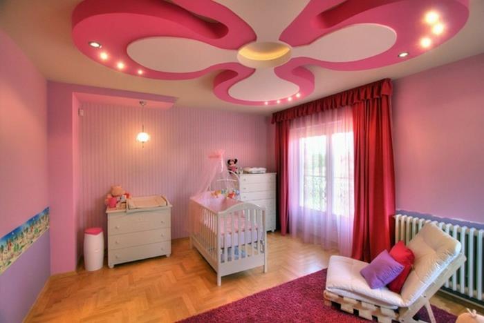 mišrus kūdikio kambario dekoras, originalios lubos, medinės grindys, kūdikio lova, fotelis ir rausvas kilimas