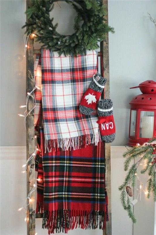 Božična obrt, enostavna božična dekoracija, ki jo naredite sami, z lestvijo, naslonjeno na steno, dve ruti z rdečimi, črno -belimi čeki, venec iz listov zelene jelke, dve rokavici v sivi in ​​rdeči barvi, majhna lučka v rdeči barvi, okrašena lestev s pravljičnimi lučmi