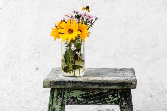 kreativna ideja, da svoj dom okrasite z recikliranimi predmeti, model starega steklenega kozarca, preoblikovanega v vazo na lesenem stolčku