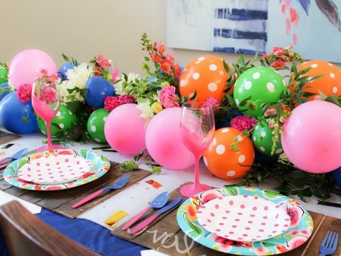 įvairių spalvų balionai, sugrupuoti į dekoratyvinę arką, rožiniai akiniai, lėkštės ir taškuoti balionai, rožės ir žalumynai