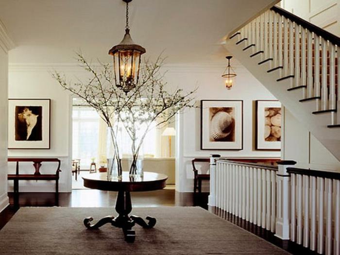 majhna okrogla miza, taupe preproga, stopnišče z belo ograjo, luč luči, ustvarijo vhod v odprt prostor