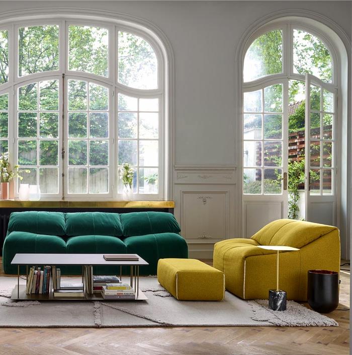 velika obokana okna v prostorni dnevni sobi z minimalistično opremo, zelena sedežna garnitura in rumena sedežna garnitura z blatom