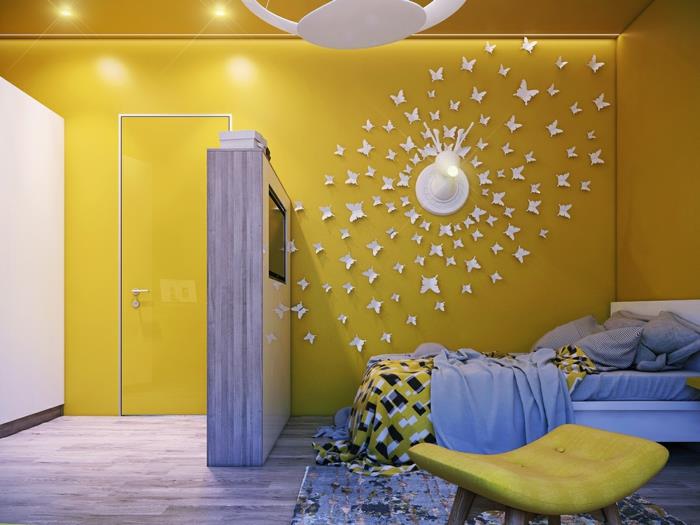 duvarları ve tavanı parlak sarıya boyanmış, zemini gri parke kaplı, duvar lambası etrafında dönen beyaz karton kelebek uygulamaları, duvar dekorasyonu, beyaz disk şeklinde tavan aydınlatması olan bir çocuk odası