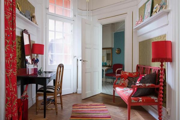 skandinaviškas dekoravimas-dryžuotas kilimas ir raudona sofa