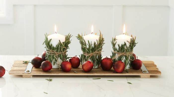 namizna dekoracija za božično leseno desko, rdeča jabolka, bele sveče, zavite z vejicami rožmarina