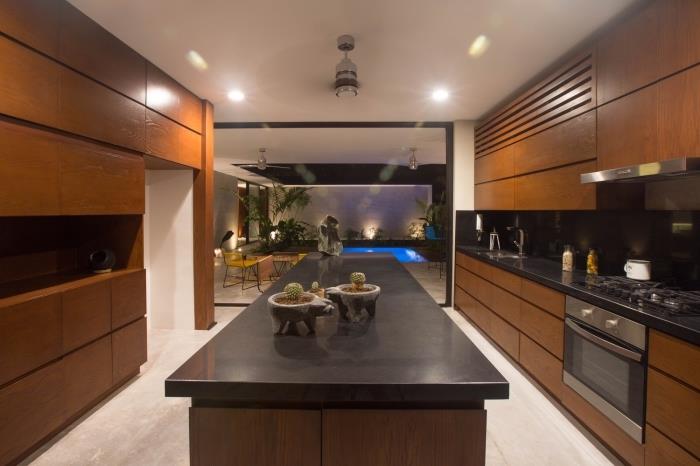 notranjost kuhinje z belimi stenami z vgrajenim pohištvom iz temnega masivnega lesa in osrednjim otokom v črnem in surovem lesu
