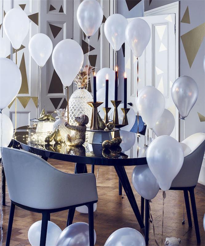 siyah masa, siyah mumlu altın mumlar, hafif çelenk ve dekoratif ananaslar, beyaz balonlar ve altın üçgenlerle süslenmiş duvarlar, zarif Yeni Yıl teması