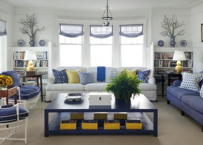 sarı desenli beyaz ve mavi, mavi ve sarı dekorlu bir İskandinav oturma odasının nasıl döşeneceği, iki kanepe, mavi ve beyaz sandalyeler, büyük sehpa, kitap rafları