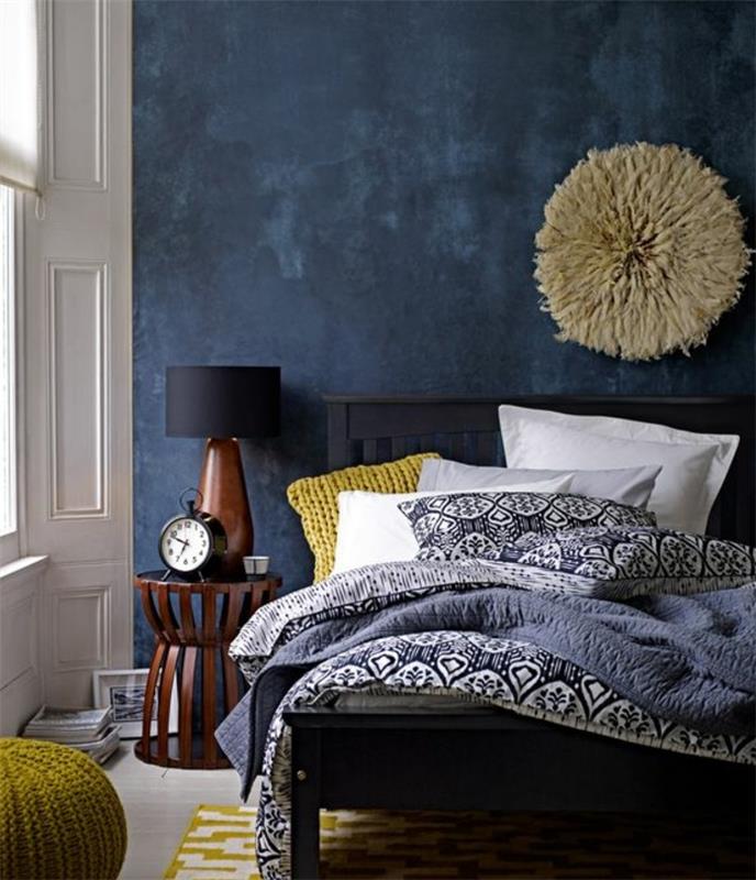 yetişkin yatak odası dekor fikri, siyah yatak, lacivert vurgulu duvar, minder, osmanlı ve sarı halı, oryantal desenli nevresimler, ilginç duvar dekoru, ahşap komidin, eski çalar saat