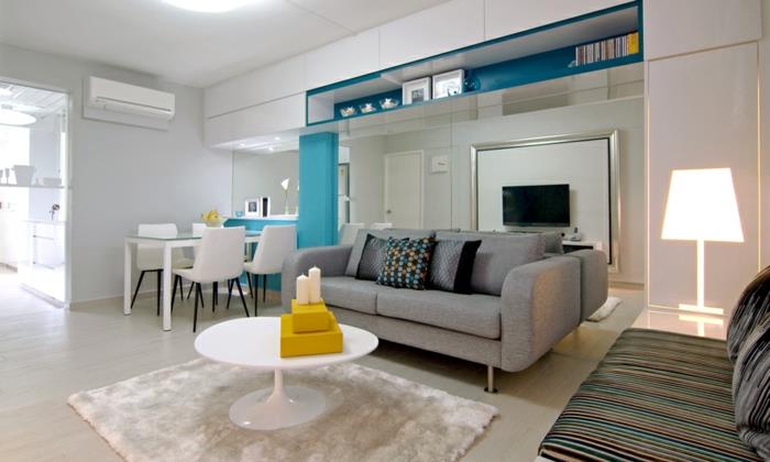 küçük mavi ve sarı dekor vurguları, gri kanepe, beyaz halı, beyaz masa, beyaz yemek alanı, küçük oturma odası, yerden tasarruf sağlayan daire
