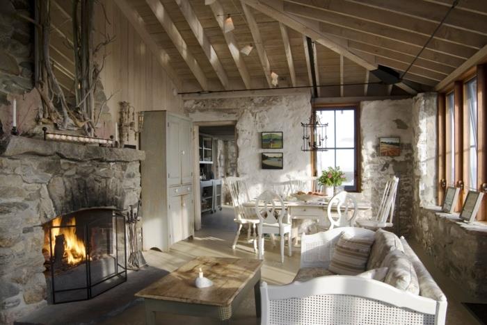 elegantna podeželska dnevna soba, lesena mizica, beli kavč, kamniti kamin, jedilnica, beli stoli in miza, siva omara