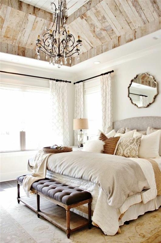 spalnica za odrasle, dežela, leseni konec postelje, bela stena, bele čipkaste zavese, baročni lestenec, okrasni leseni strop iz deske, sivo, belo in bež posteljnina