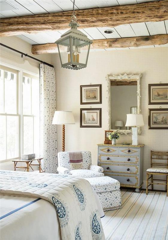 dekor za spalnico v slogu podeželskega sloga, izpostavljeni tramovi, starinska pastelno modra komoda, belo in modro posteljno perilo, viseča luč, črtasta preproga, kavč, blato in zavese s cvetličnim vzorcem