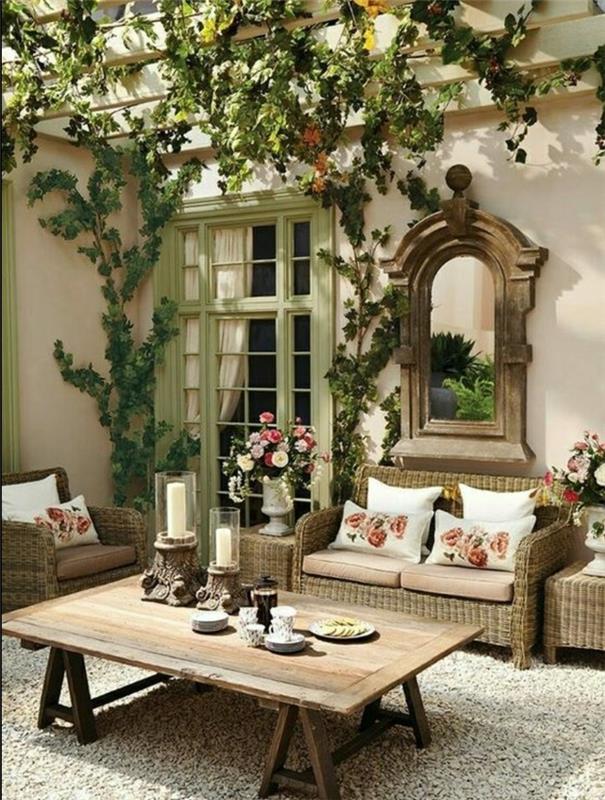 elegantna podeželska dekoracija na prostem, lesena mizica, fotelj in kavč iz ratana, siva preproga, blazine za svobodo in cvetlični okras