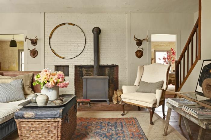 stalas iš rotango spintelės, odinė sofa, senovinis židinys, retro fotelis, senovinis rytietiškas kilimas, elnių ragų apdaila, kaimiška svetainė