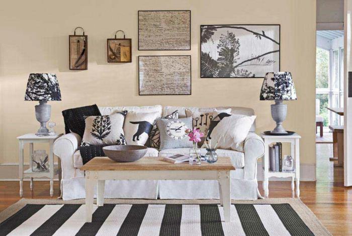 bel kavč, lesena mizica, črtasta preproga, črno -belo, blazine v sivi, beli in črni barvi, stena v bež barvi, svetel parket, dekoracija sten
