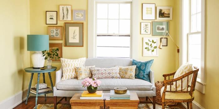 eleganten podeželski dekor, svetlo rumena stena, siv kavč, klubska mizica in leseni stol, večbarvne blazine, dekorativne stenske slike