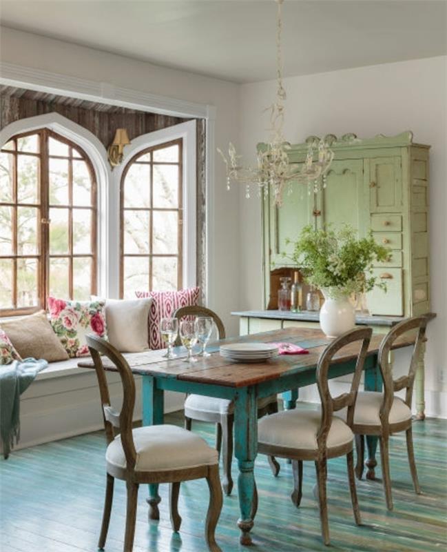 Ideja za dekoracijo podeželskega šika, jedilnica, lesena miza, prebarvana v modro, leseni stoli, okenski sedež, večbarvne blazine, omara za pistacije