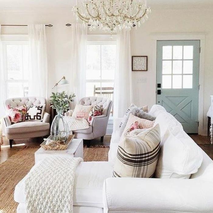 dekor podeželske dnevne sobe, beli kavč, blazine vzorca Liberty, kvačkana pletenica, umazano bele zofe, pastelno modra vrata, baročni lestenec