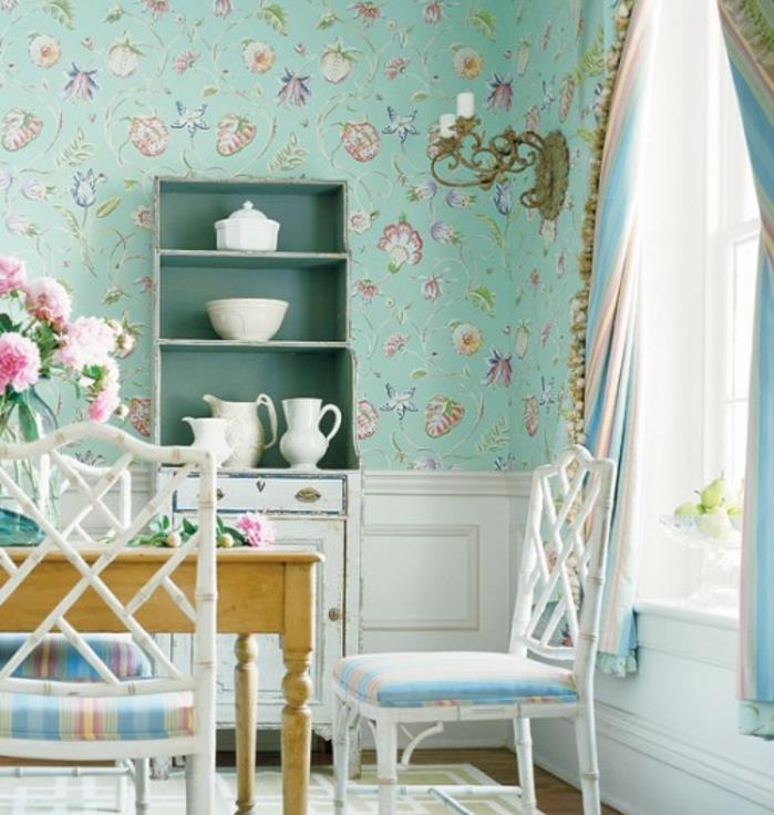 Ideja dekorja country chic, pastelno modra ozadja s cvetličnimi vzorci, patiniran beli predalnik, lesena miza in stoli, črtast tekstil, šopek rožnatih potonik