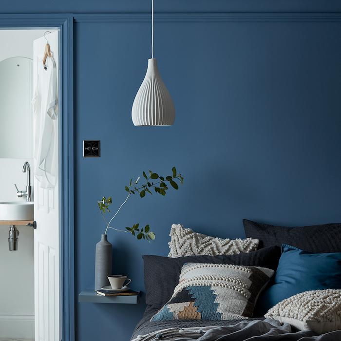 modra barva stene pantone, blazine temnih tonov na postelji s sivim posteljnino, belo vzmetenje