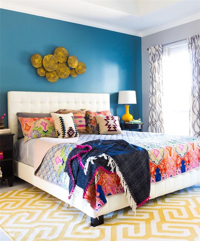 dekor glavne spalnice z modro steno, pisano posteljnino s cvetličnimi vzorci, boemski šik slog, bela in rumena preproga