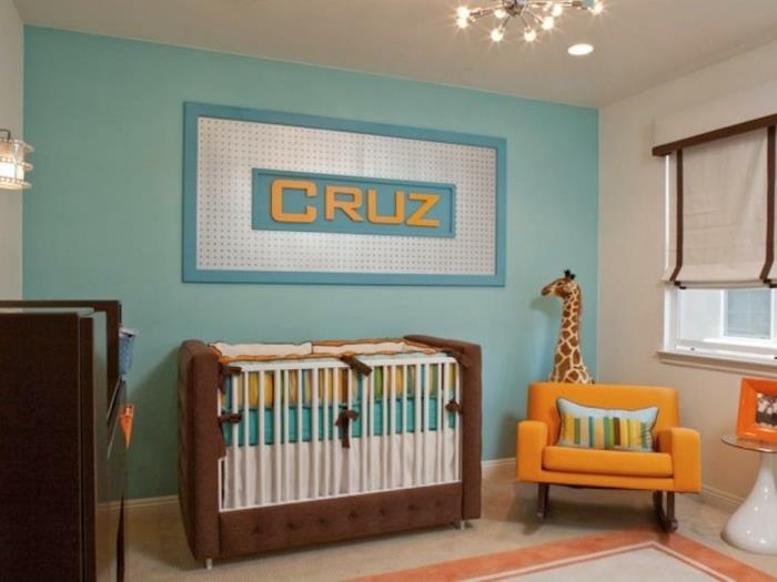 kūdikio berniuko kambario dekoras, mėlyna siena, oranžinis fotelis, didelė kūdikio lova, sienų dekoras