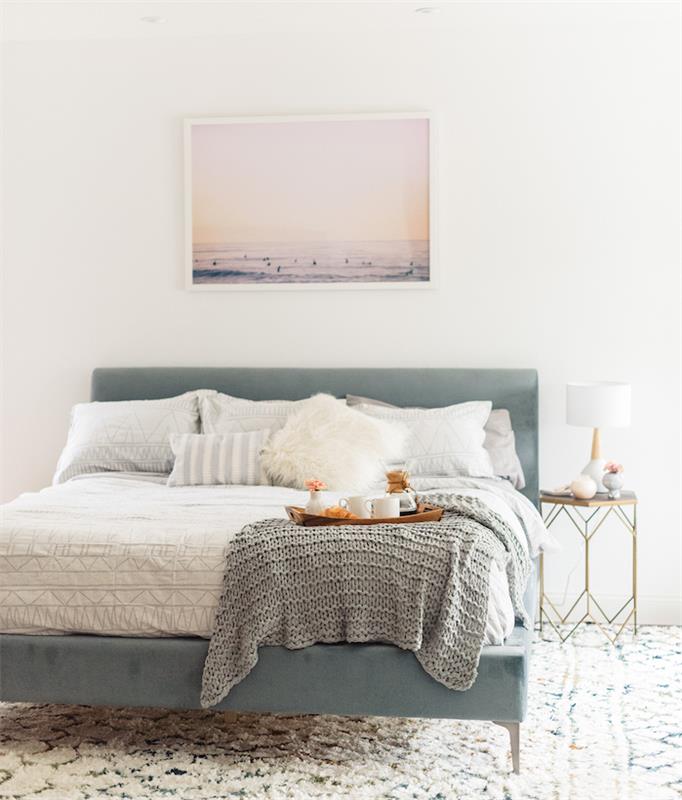 Ideja za dekoriranje spalnice v kokonu, bela preproga z geometrijskimi vzorci, pastelno modra postelja, belo in sivo posteljnina, siva pletena pletenina