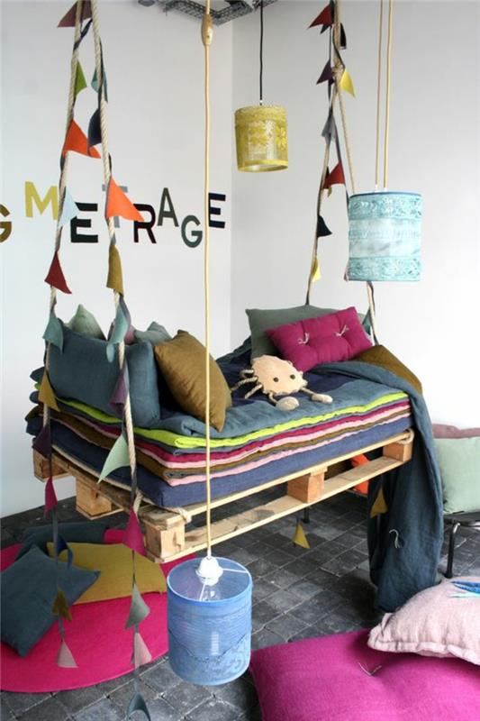 mergaitės kambarys, sūpynės, pakabintos nuo lubų, pagamintos iš padėklų, papuoštos įvairiaspalvėmis vėliavomis, perlinės pilkos plytelės, grindys padengtos pagalvėlėmis ir ryškiomis spalvomis