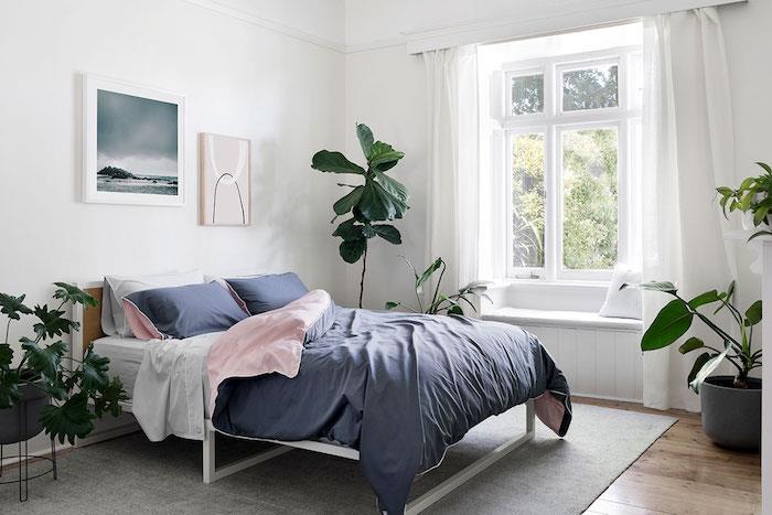 dekor spalnice v džungli z zelenimi rastlinami v posteljni posodi, lesenim parketom, sivo preprogo ter sivo -rožnato črto