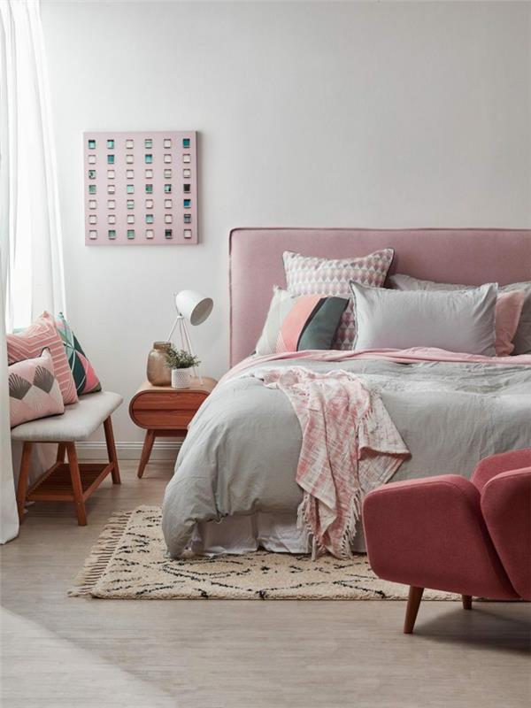 Berberų kilimas, pilka ir rožinė lova, rožinis fotelis, medinis naktinis stalas, rožinė audinio galvutė, šviesiai pilki suaugusiųjų miegamojo dažai