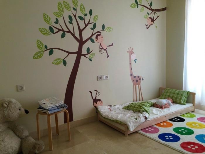 medinė lova ant grindų, medžio darželio lipdukai, beždžionės, įvairiaspalviai kilimėliai sagomis, meškiukas, Montessori kūdikio lovos idėja
