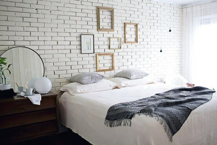 stena pravokotnih okvirjev in uokvirjena risba, opečna stena, lesena nočna omarica, belo in sivo posteljnina, skandinavska dekoracija spalnice