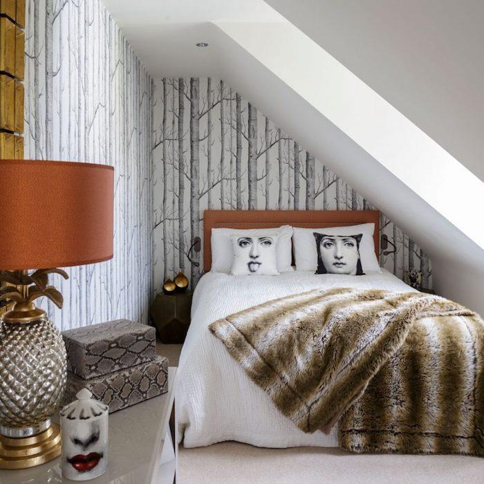 yokuş altı yatak odası dekoru örneği, İskandinav duvar kağıdı ile süslenmiş duvar, beyaz keten ile ahşap yatak, suni kürk battaniye, yılan desenli saklama kutuları