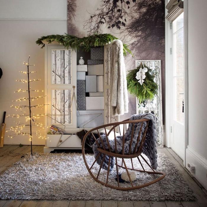 prepredena preproga v hiši Hygge, leseni gugalnik, siva debela karirasta, bela garderobna omara, božično drevo z lahkim vencem, okrasna plošča z nordijskim gozdnim vzorcem