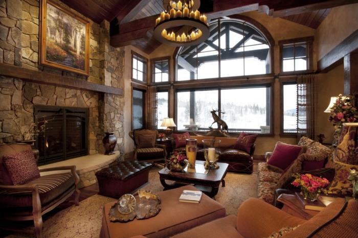 šiuolaikiškas kaimiško stiliaus dekoras, odinė sofa, rudas fotelis, medinė kėdė, akmeninis židinys, liustra su žvakėmis, senovinis kilimas, medinis kavos staliukas, vaizdas į kalnuotą kraštovaizdį
