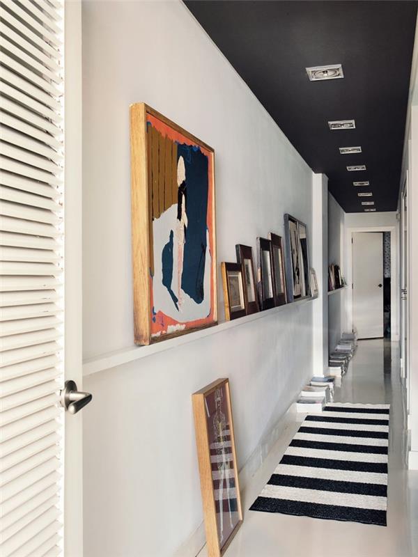 dolga in ozka dekoracija hodnika v črno -beli barvi s polico umetniških okvirjev in mat črno pobarvanim stropom za lep grafični učinek