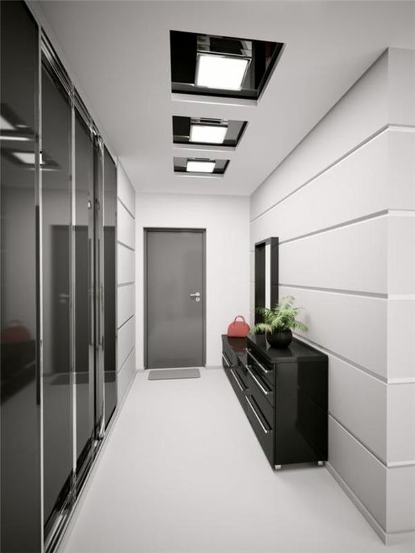 ilgas ir siauras juodos ir baltos spalvos koridorius su blizgiais paviršiais, juodos ir baltos spalvos kvadratinės formos lubų šviestuvai, juoda įėjimo spintelė su lygiu blizgiu paviršiumi, lygios baltos grindys