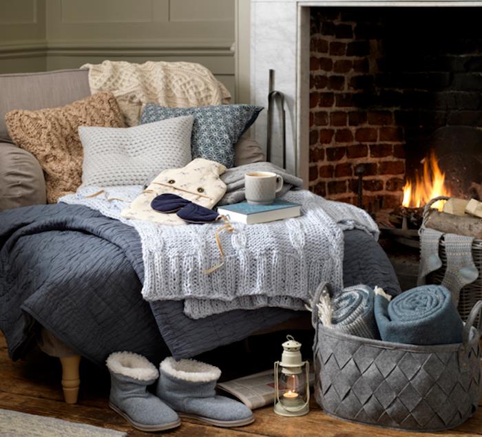 jaukus žiemos dekoras, tekstilė, antklodės, pledai ir pagalvėlės mesti ant jaukios pilkos sofos, žieminės šlepetės, tekstilės laikymo krepšelis, medžio parketas