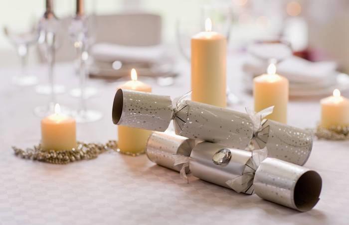 topovi konfeti in venec iz kroglic okoli sveč različnih velikosti na sivo -belem prtu