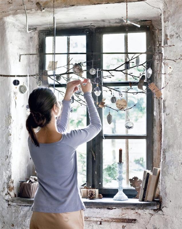 Kalėdinė dekoracija, pagaminta iš medžio, nuoga šaka, pakabinta horizontaliai ir papuošta kalėdiniais ornamentais, kad būtų sukurta originali lango puošmena žiemai