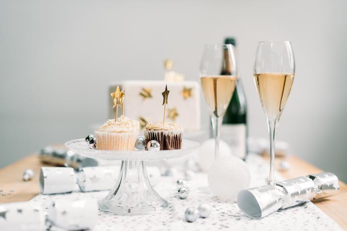 konfeti topları, gümüş yıldızlı beyaz masa örtüsü, servis tepsisinde kekler, şampanya bardakları