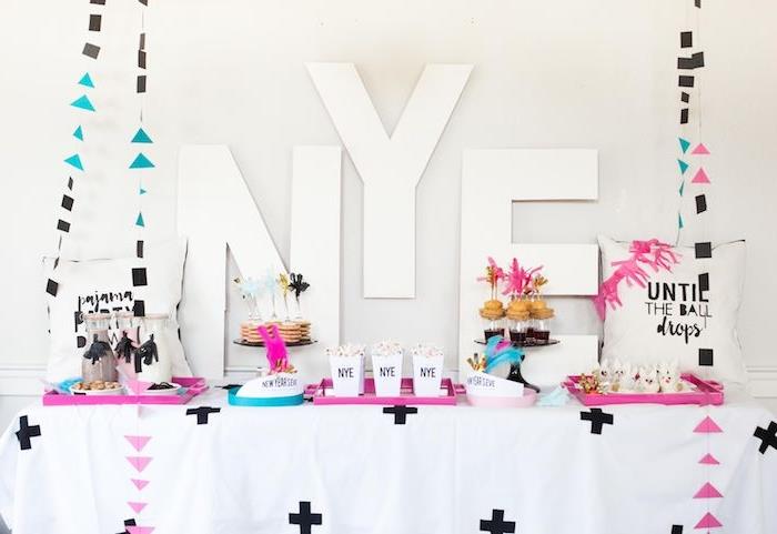 novoletne črke na ozadju, miza z rožnatimi in modrimi pladnji za serviranje, venci z geometrijskimi figurami, mini novoletne palačinke s sladkarijami