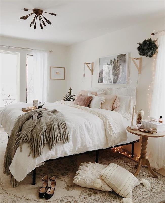 minkšta pilka antklodė ant rožinės ir baltos eilės lovos, baltos ir rožinės pagalvėlės, baltos sienos, dekoratyvi šviesi girlianda, kokoninis kilimas, romantiškas moteriškas miegamojo dekoras