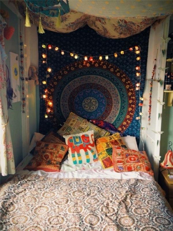 bohemiškas miegamojo dekoras, smėlio spalvos lovos metimas, etninių raštų pagalvėlės, šviesi girlianda